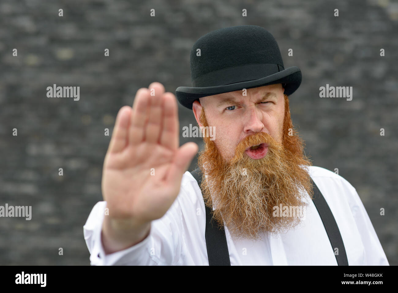 Bearded man in bowler hat and braces giving a stop sign or gesture with