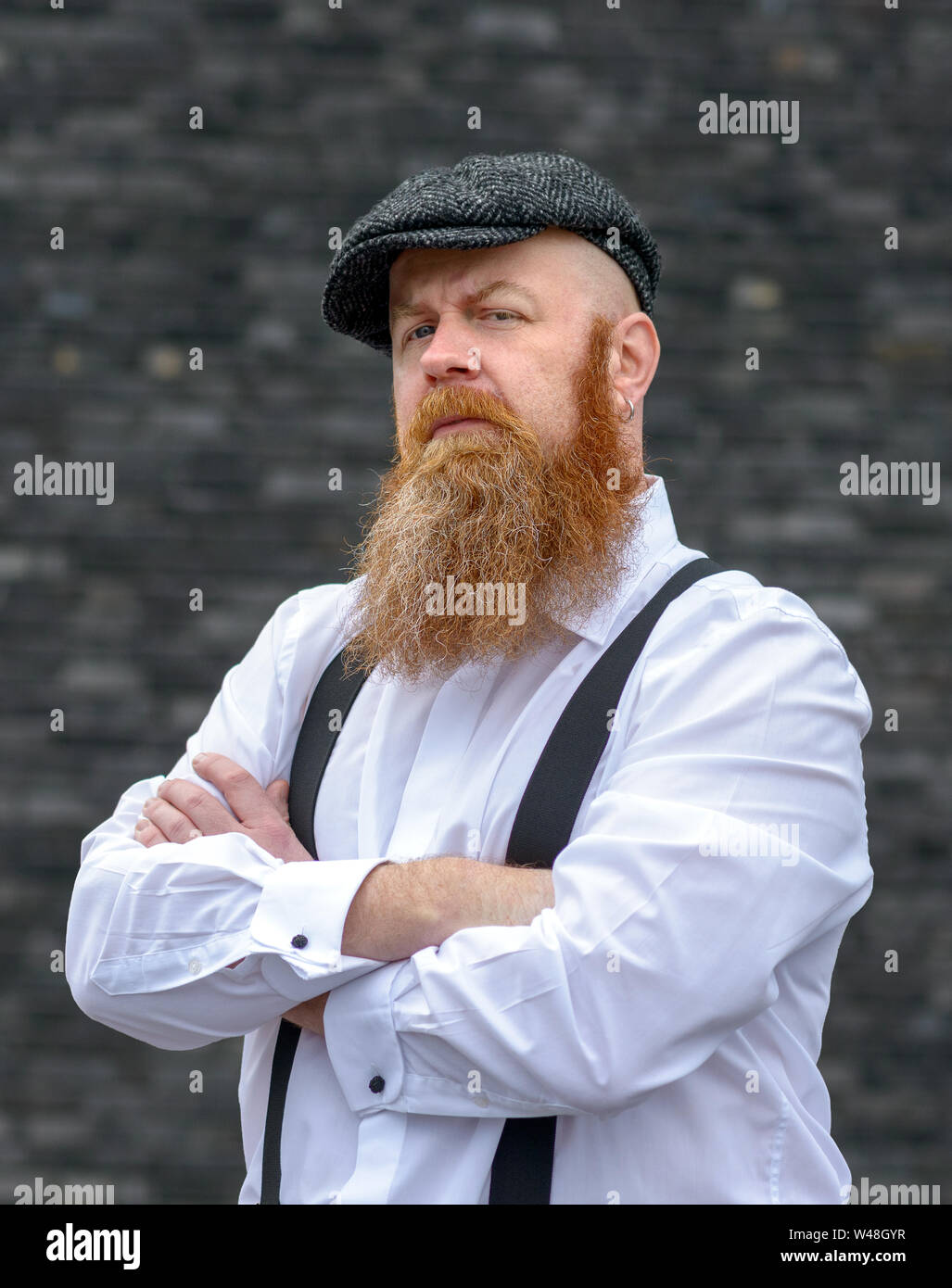 Portrait of a overweight bearded man in cloth hat and braces standing with  folded arms Stock Photo - Alamy
