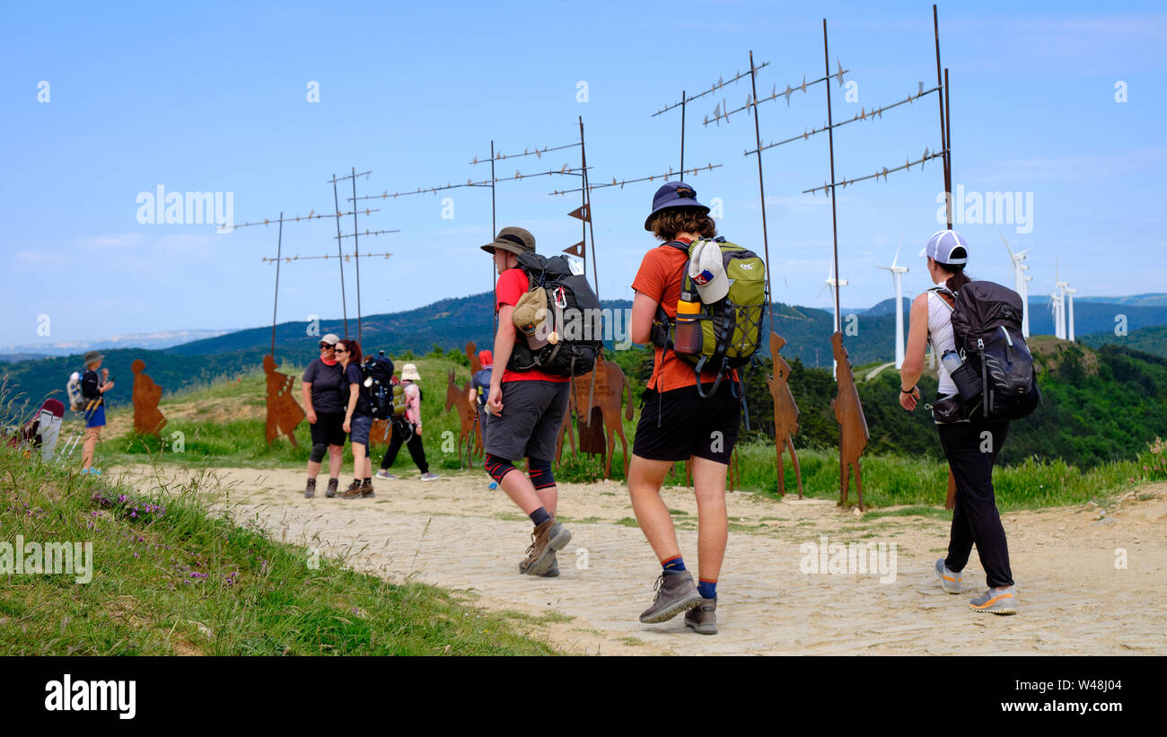 Pilgrims walking on the Camino de Santiago. Walkers arriving at the monument at the top of the Alto del Perdon, while other take photo on their break Stock Photo