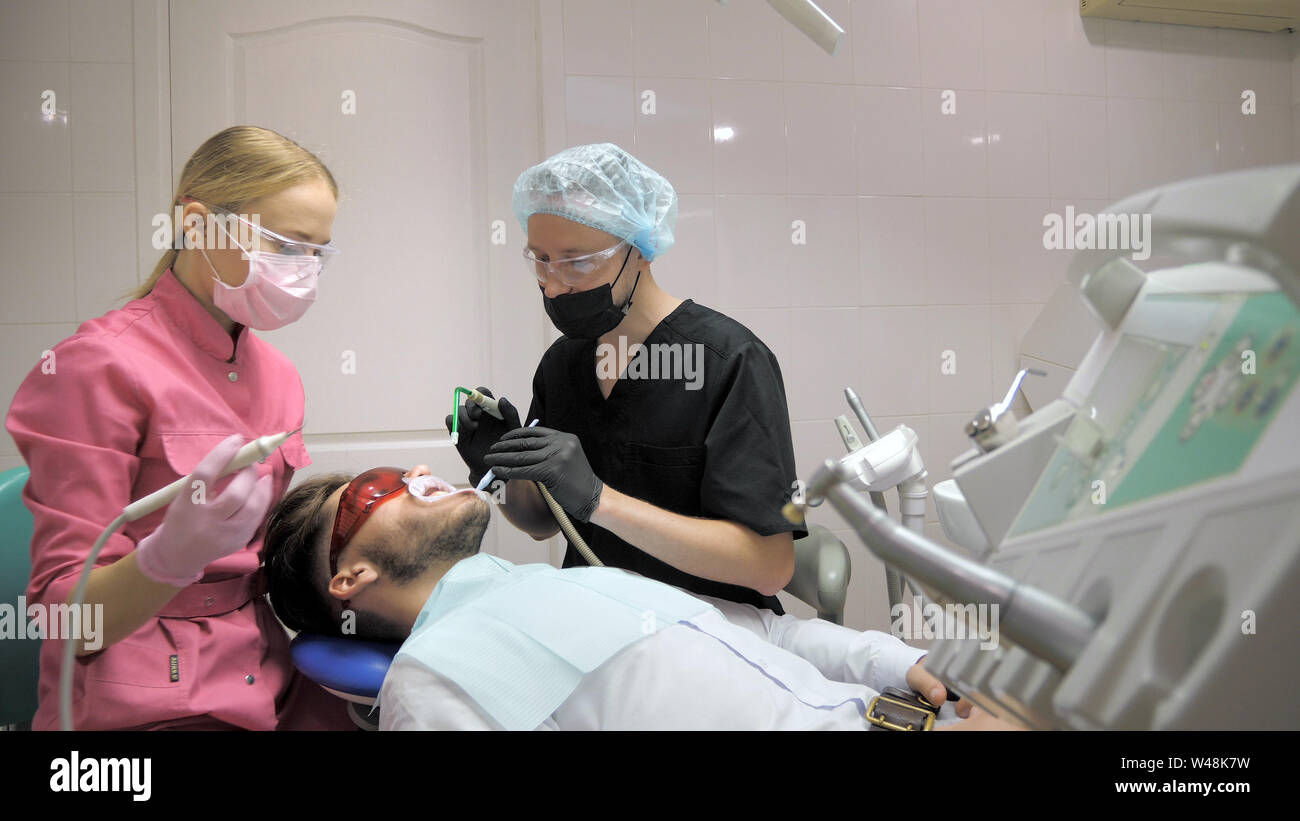 Female dentist with male patient doing the cleaning of the tooth in