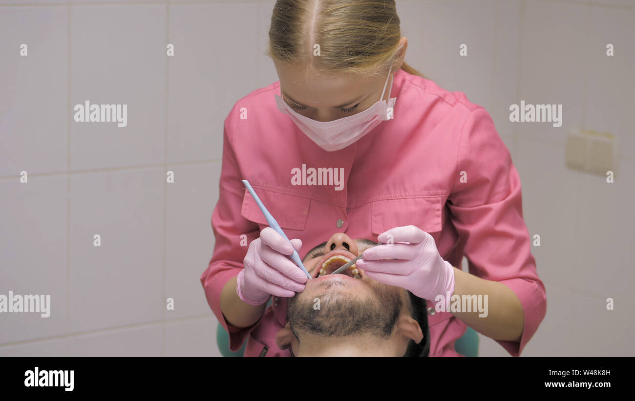 Female dentist with male patient doing the cleaning of the tooth in