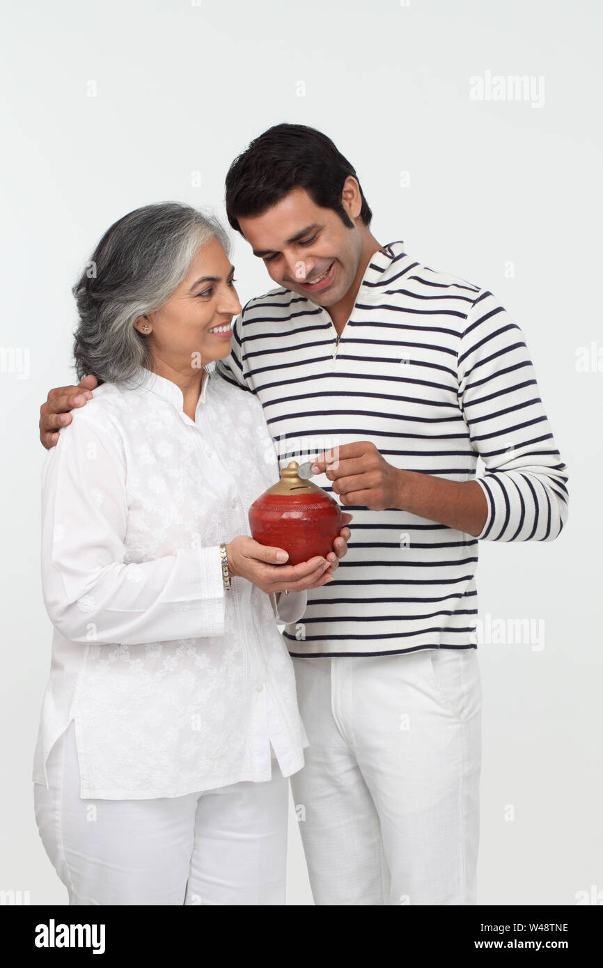 Man putting coin into a piggy bank with his mother Stock Photo - Alamy