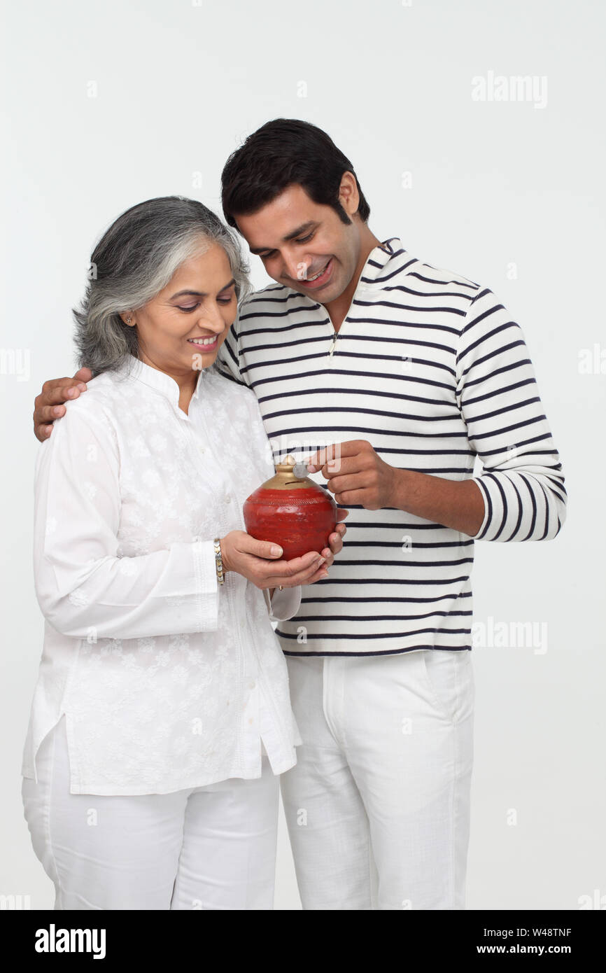 Man putting coin into a piggy bank with his mother Stock Photo - Alamy