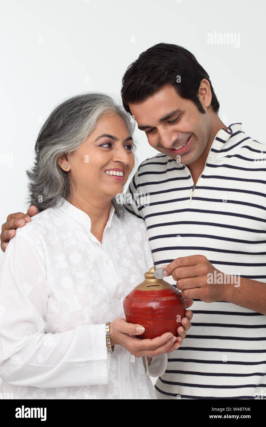 Indian man putting coin into a piggy bank with his mother Stock Photo ...