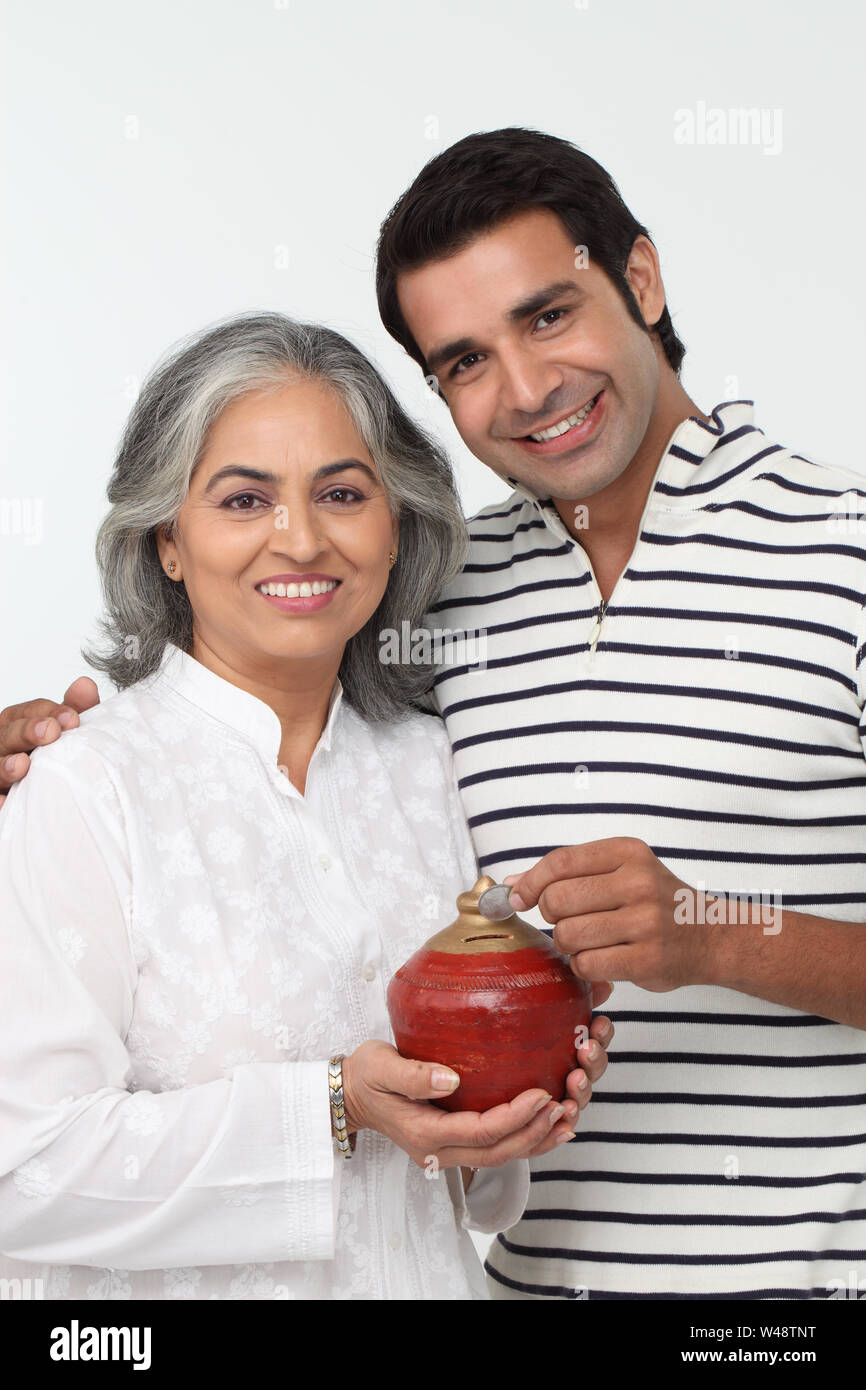 Man putting coin into a piggy bank with his mother Stock Photo - Alamy