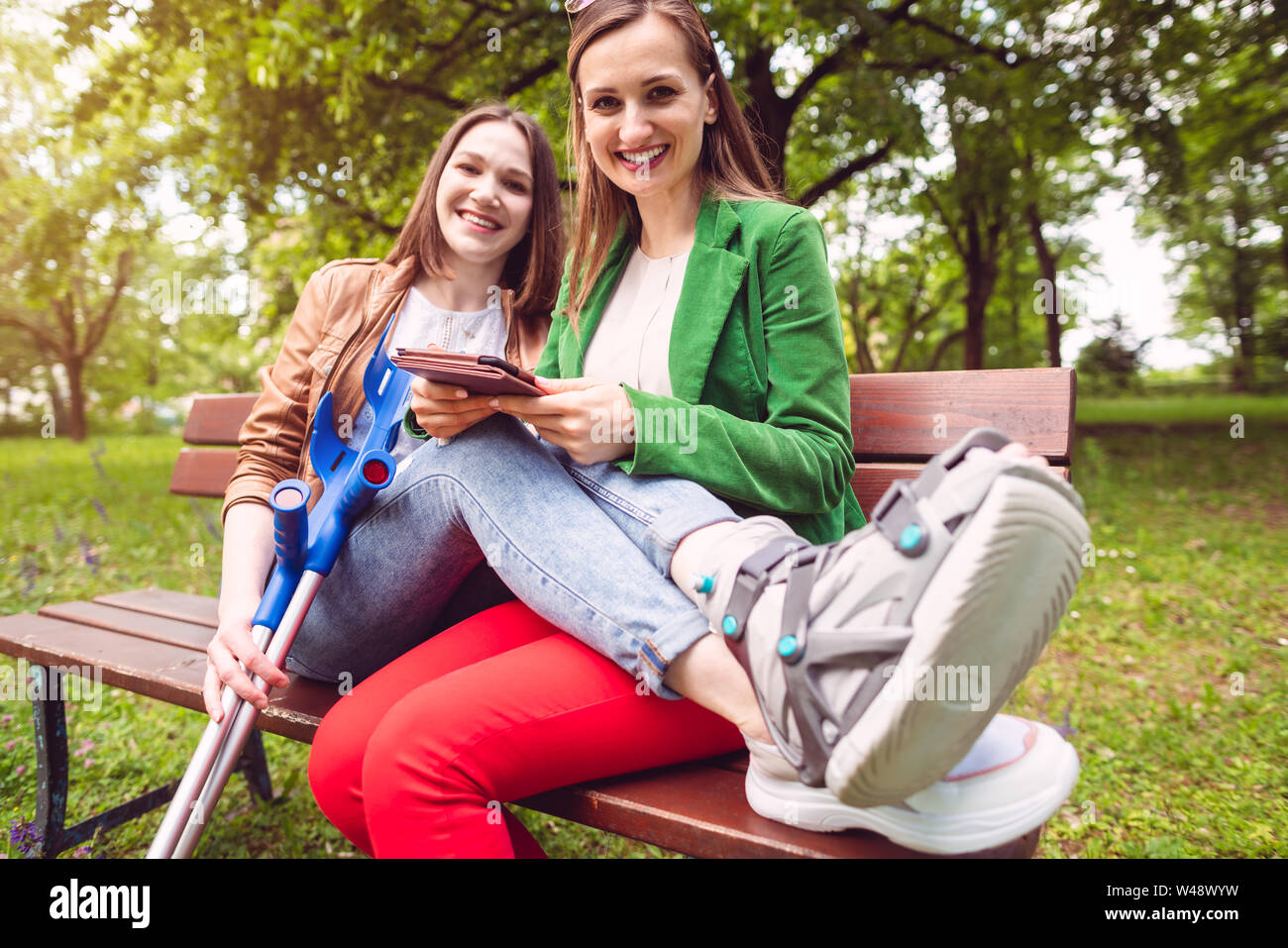 Two best friends, one with an injured leg, reading a book Stock Photo