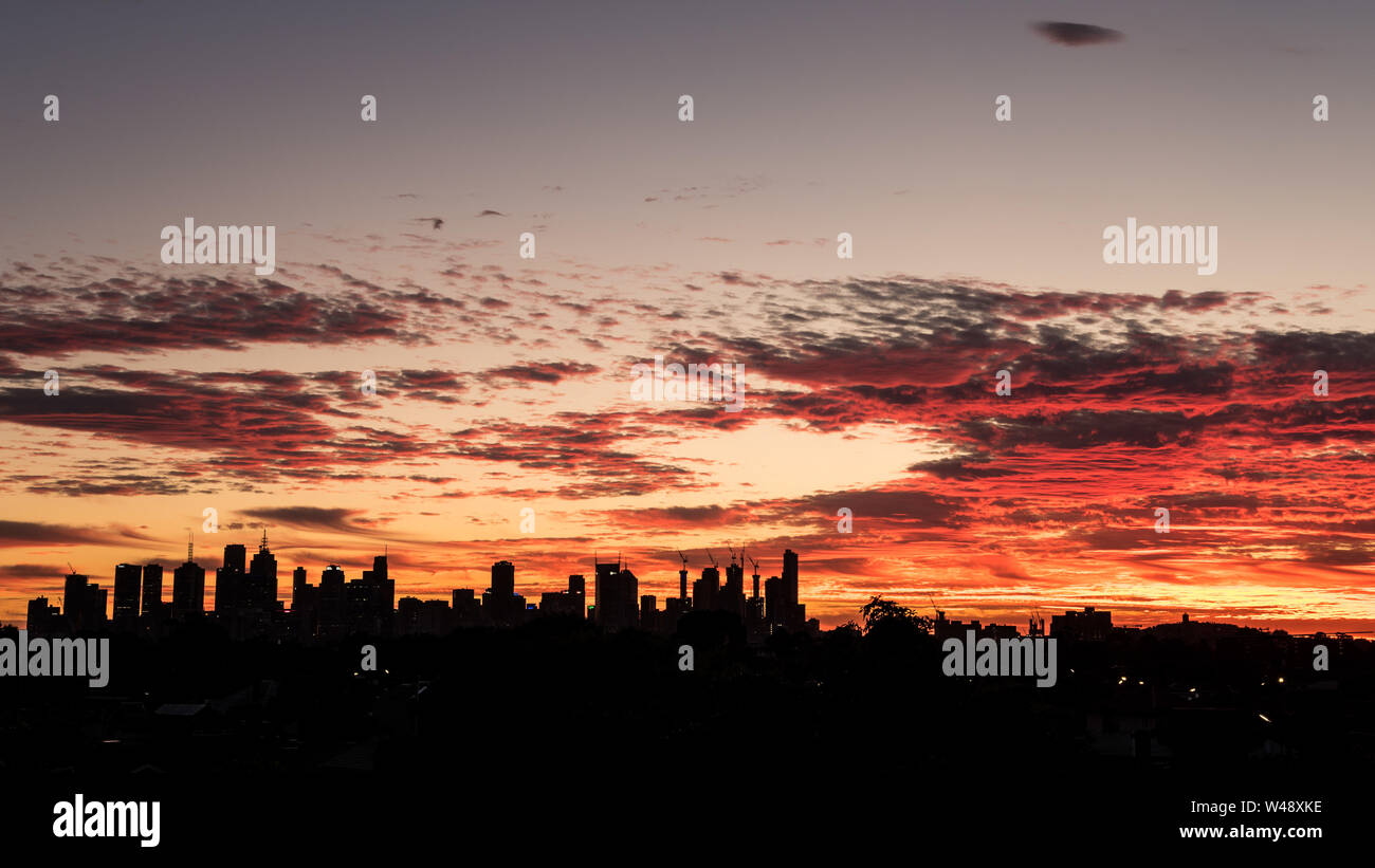 Skyline of the city of Melbourne at sunset with the dark shape of the buildings contrasting with the red and orange colors of the clouds in the sky. Stock Photo