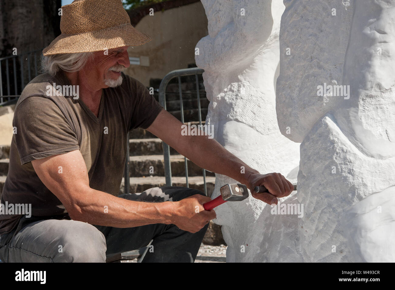 Senior sculptor working outdoor on his marble sculpture in his workshop with hammer and chisel Stock Photo