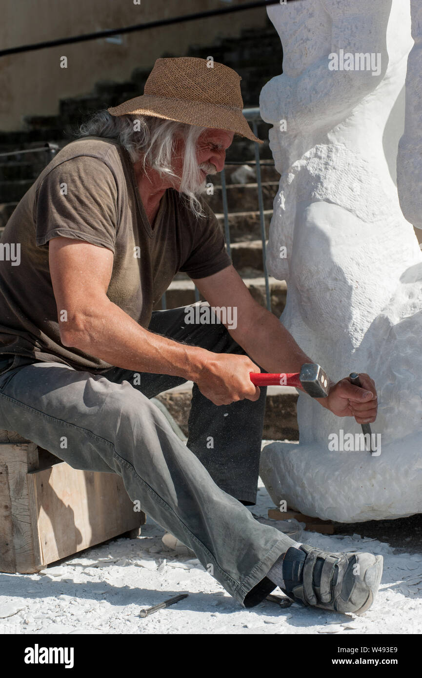 Senior sculptor working outdoor on his marble sculpture in his workshop with hammer and chisel Stock Photo