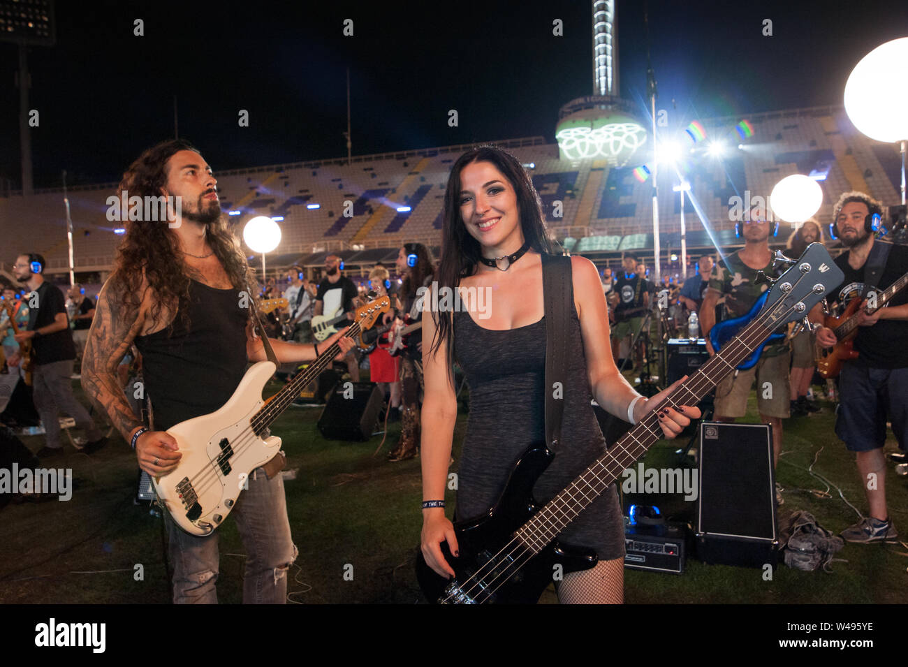 Florence, Italy - 2018, July 21: Young beautiful woman with electric bass and other musicians at the city stadium arena during the “Rockin’1000 - That Stock Photo