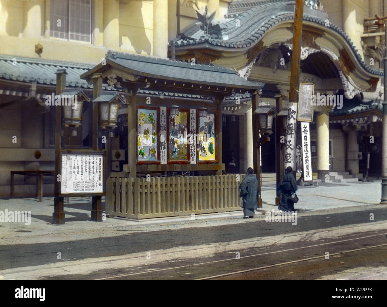 [ 1910s Japan - Tokyo Kabuki Theater ] —   Two Japanese women in front of Kabukiza, a theater for kabuki performances, in Ginza, Tokyo. The original Kabukiza was established in 1889 (Meiji 22). It was replaced with the building on this image in 1911 (Meiji 44). This structure was destroyed by fire in 1921 (Taisho 10), after which a new building was built in baroque Japanese revivalist style. This was demolished in 2010 (Heisei 22) to make way for a larger modern structure. The theater has been run by the Shochiku Corporation (松竹株式会社) since 1914 (Taisho 3).  20th century vintage glass slide. Stock Photo