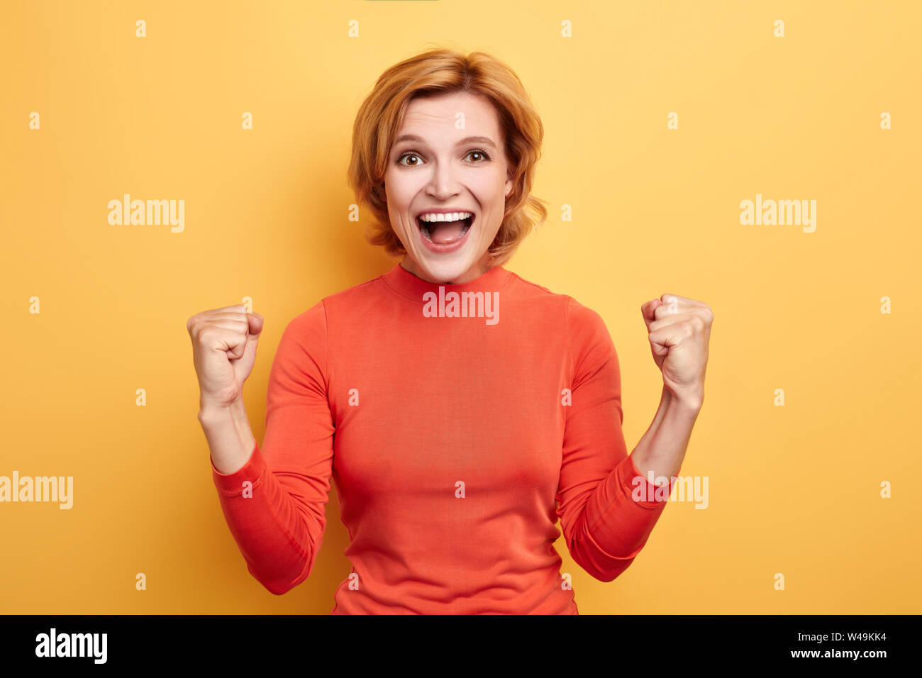 awesome girl in red stylish roll-neck sweater rejoicing at the victory of her favourite team. fan concept. isolated yellow background Stock Photo