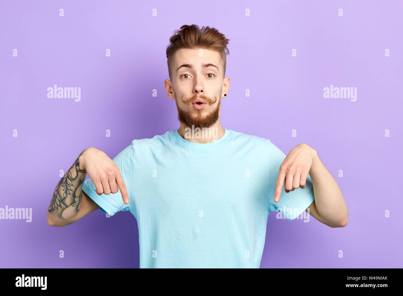 bearded handsome man indicates down as shows something, , isolated over blue concrete wall.close up portrait. studio shot.body language. Stock Photo