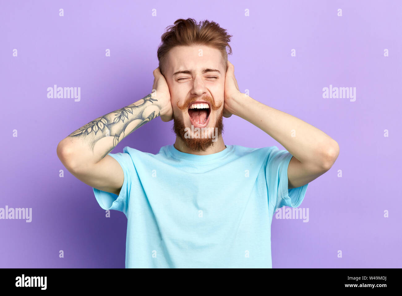 frustrated nervous annoyed young man with wide open mouth closing ears