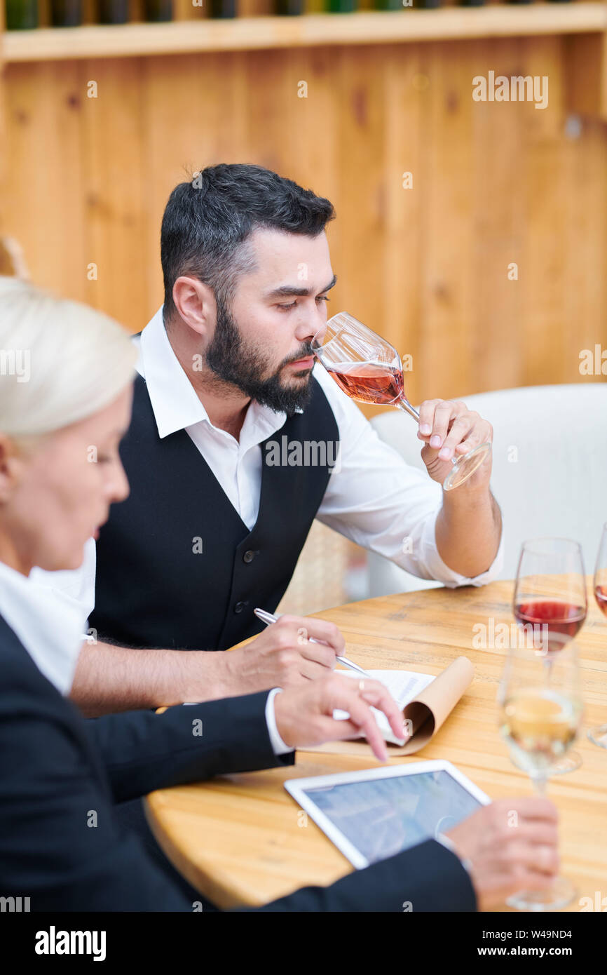 Bearded young man in formalwear smelling various sorts of wine Stock Photo