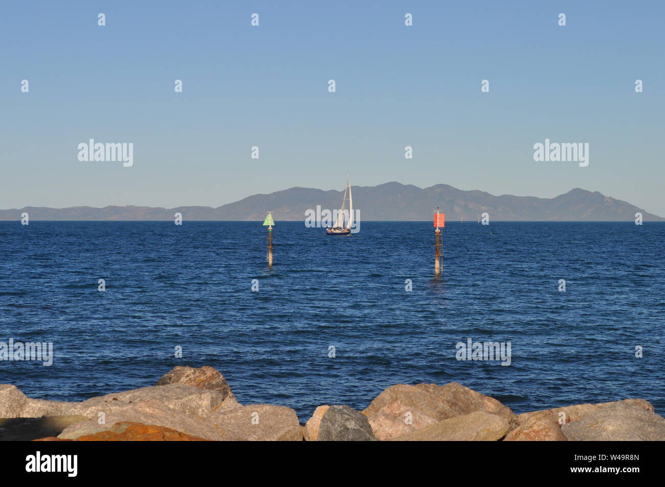 View from the breakwater at Nelly Bay on with marina channel markers, a yacht, and the coast of Australia near Townsville beyond. Stock Photo