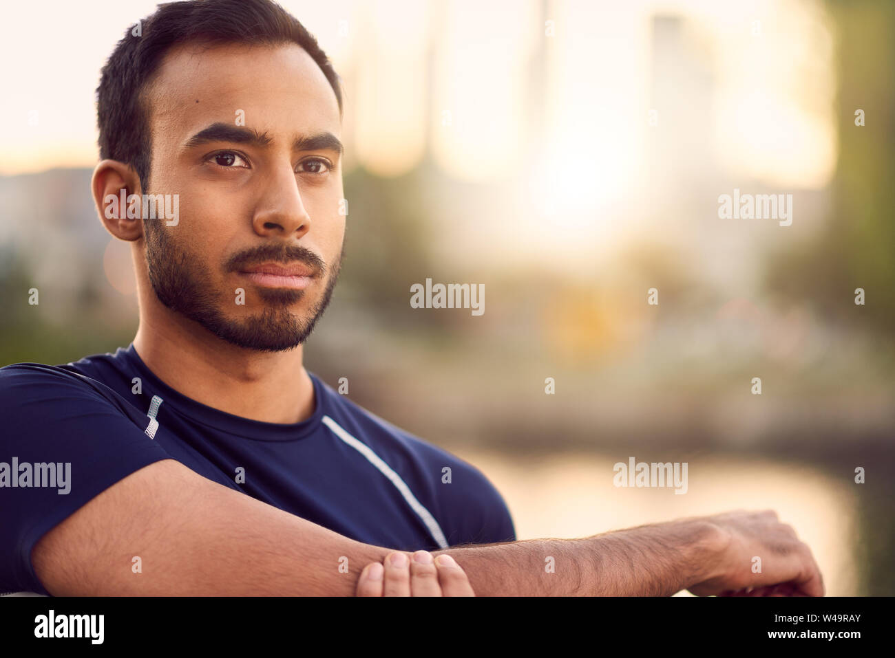 Portrait of active millenial man jogging at dusk with an urban cityscape and sunset in the background Stock Photo