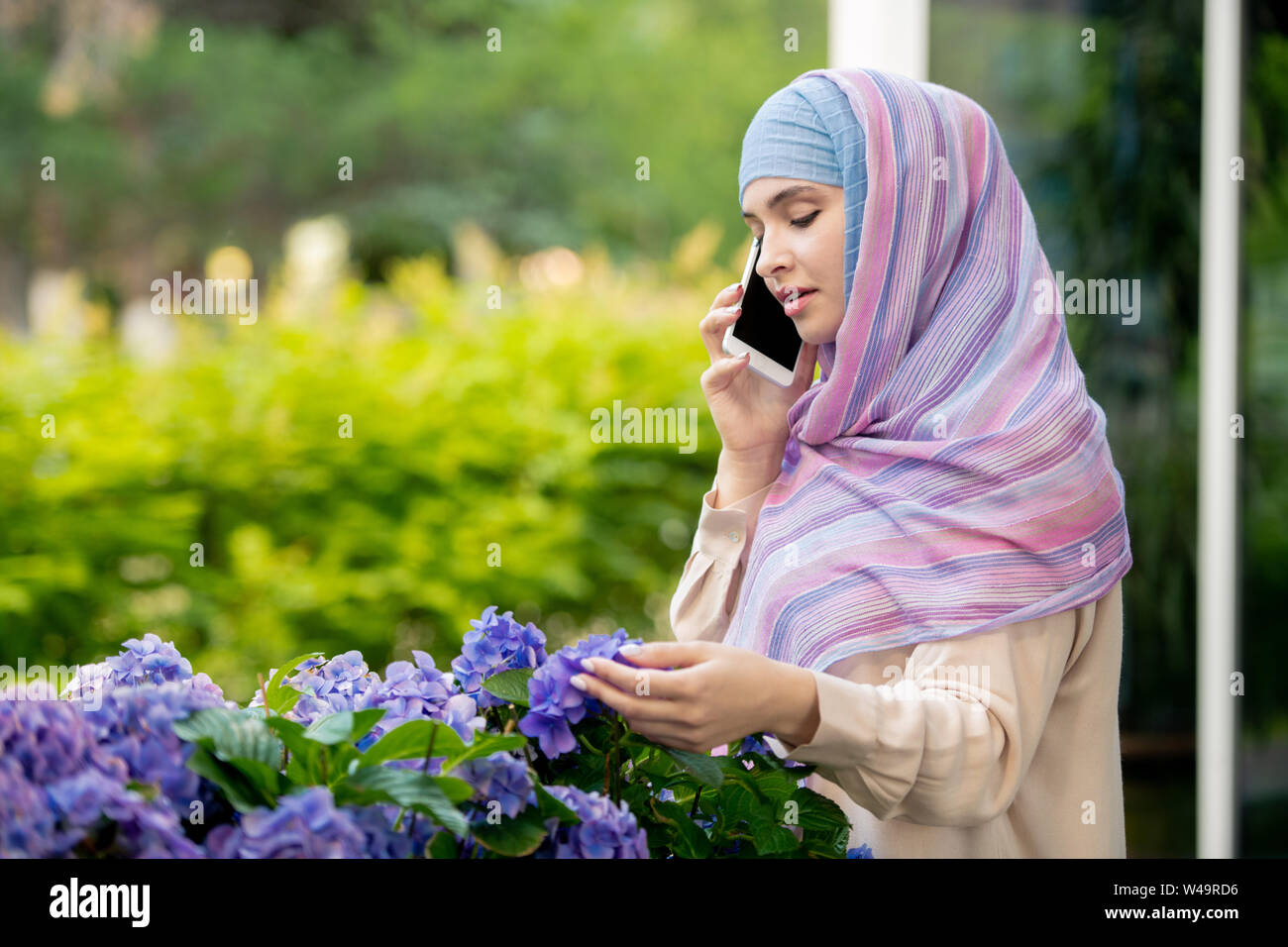 Young muslim woman in hijab talking on smartphone by flowerbed Stock ...