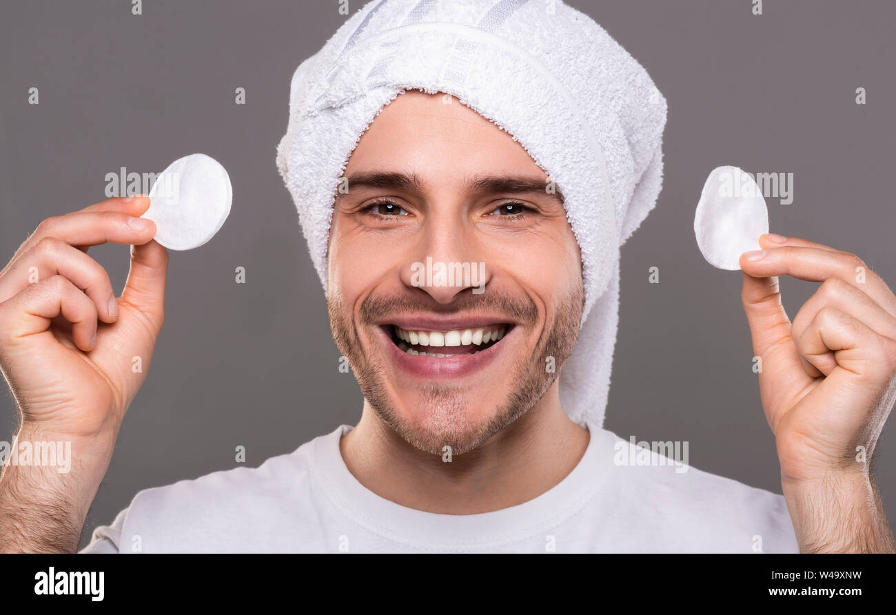 Young man with cleaning face with cotton pads with towel on his head
