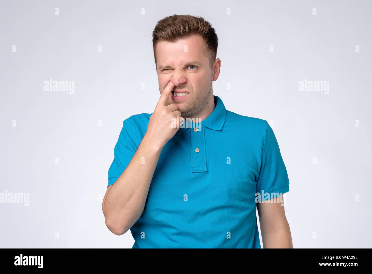 Young caucasian man in blue shirt picking in his nose. Stock Photo