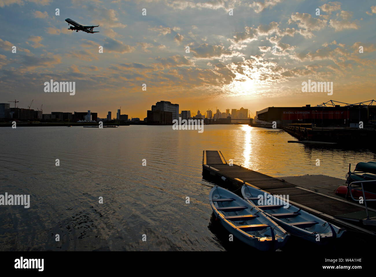 Sunset over the Emirate Royal Docks. Looking west from Connaught Bridge towards central London. An aircraft on final approach th London City Airport Stock Photo