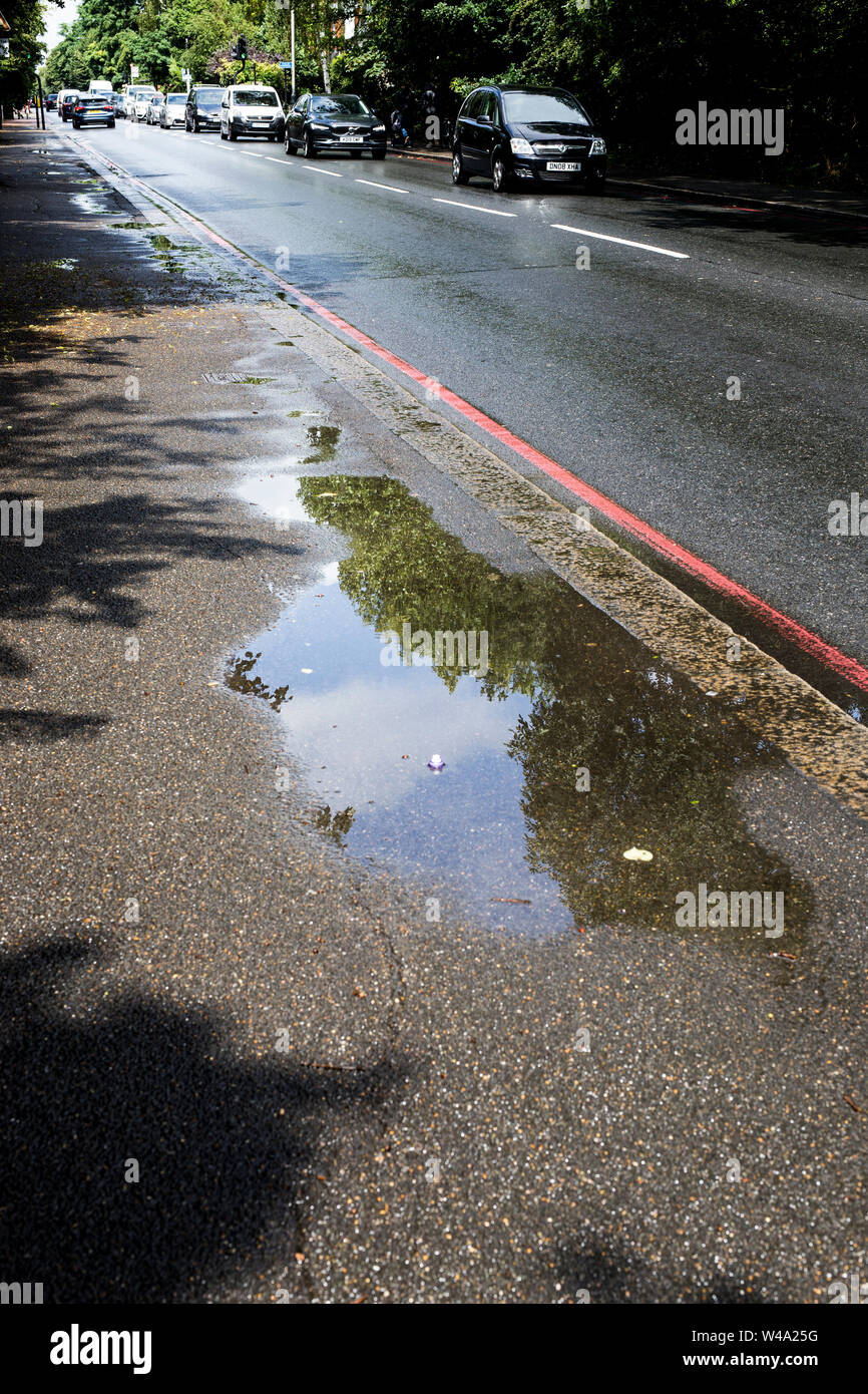 Reflection in puddle on pavement next to road running through Wandsworth Common, London. Stock Photo