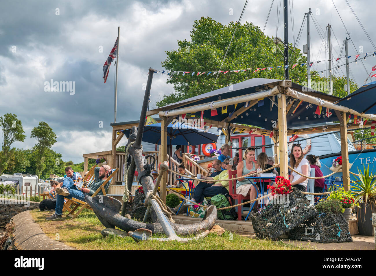 Watermouth Harbour, Berrynarbor, near Ilfracombe, North Devon, UK. Sunday 21st July 2019. UK Weather.  Despite the gathering cloud holidaymakers enjoy the long sunny intervals and admire the view over Watermouth Harbour as they take refreshments at the 'Storm in a Teacup cafe'. Credit: Terry Mathews/Alamy Live News Stock Photo