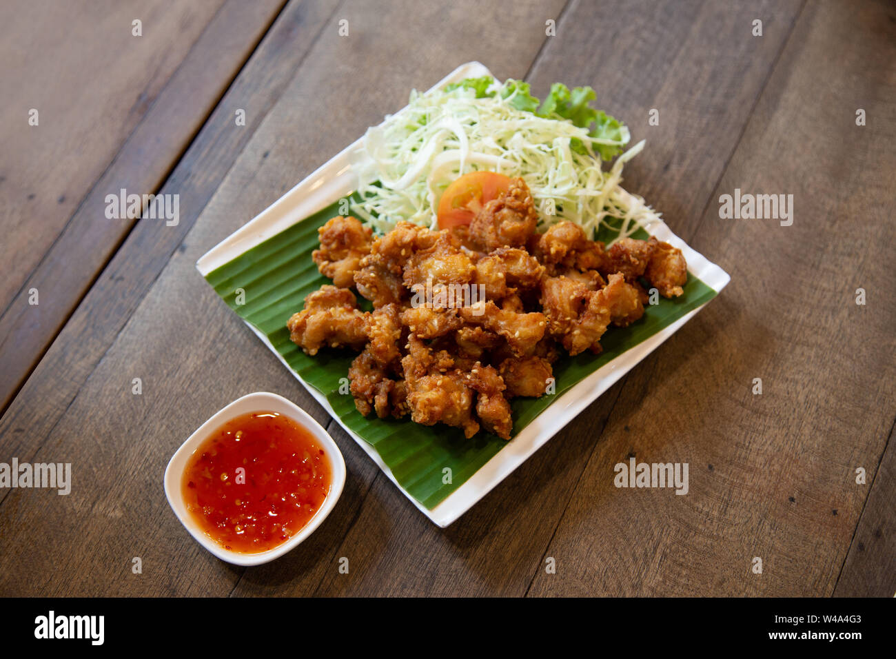 crispy chicken leg grilled in Thai style serve with spicy sauce and tomato and vegetable on green banana leaf Stock Photo