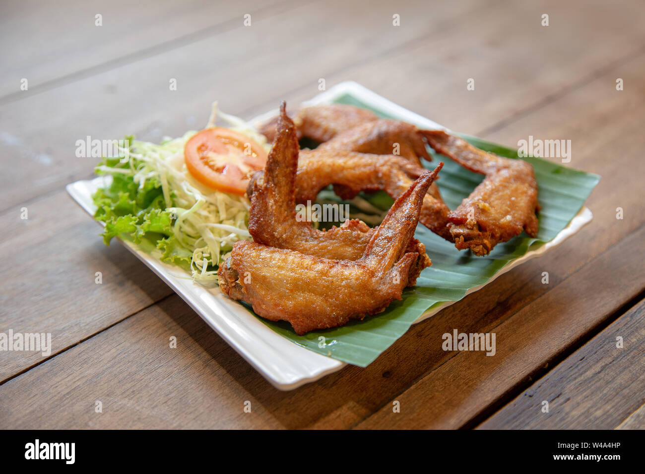 crispy chicken wing grilled in Thai style serve with tomato and vegetable on green banana leaf Stock Photo