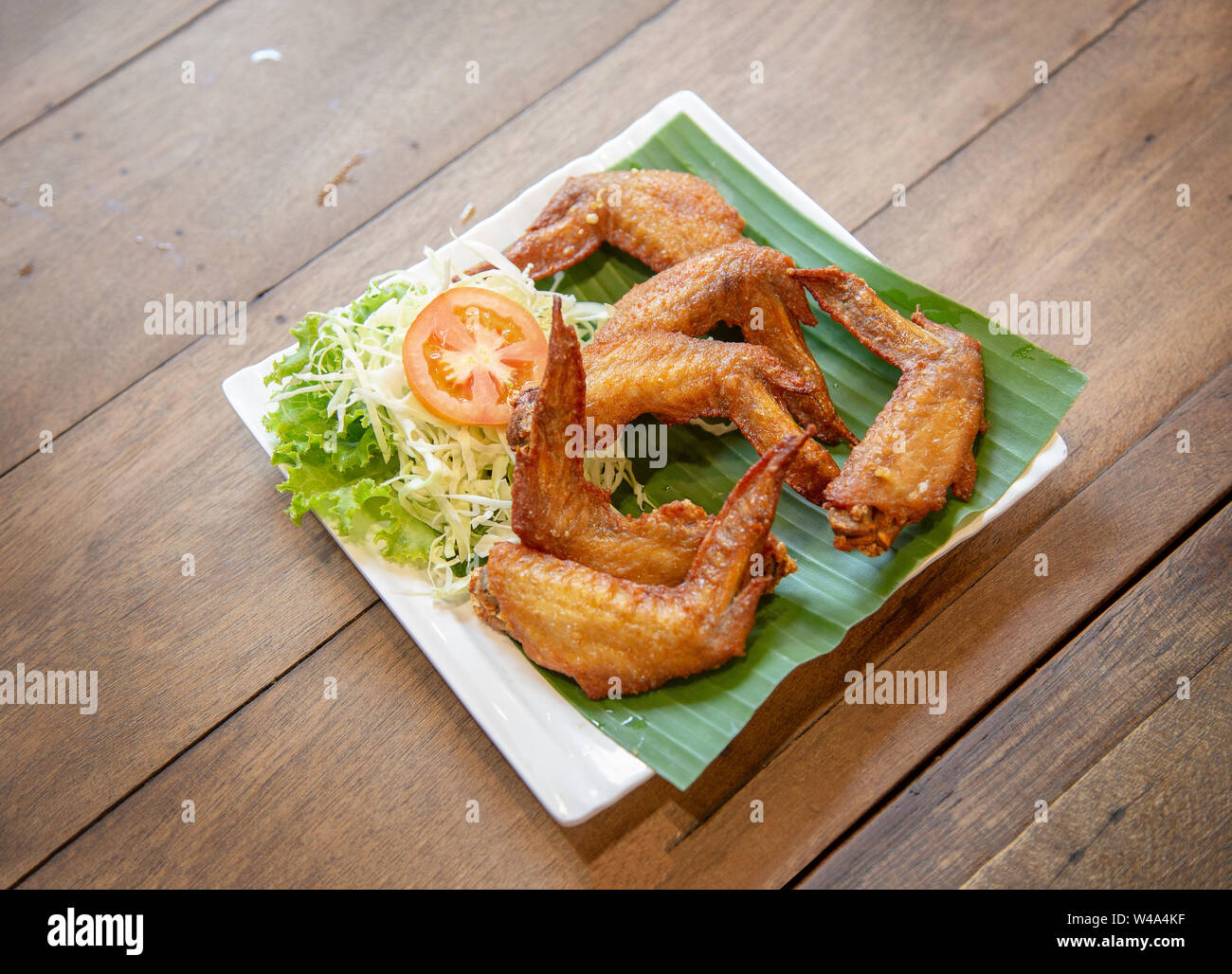 crispy chicken wing grilled in Thai style serve with tomato and vegetable on green banana leaf Stock Photo