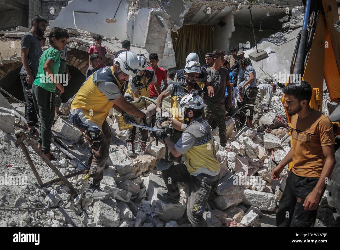 Urm Al Jaws, Syria. 21st July, 2019. Members of the Syrian Civil Defence also known as 'White Helmets' carry a victim after a building collapsed during a reported air strike by pro-regime forces in the town of Urm Al-Jaws in the south of Idlib. Credit: Anas Alkharboutli/dpa/Alamy Live News Stock Photo