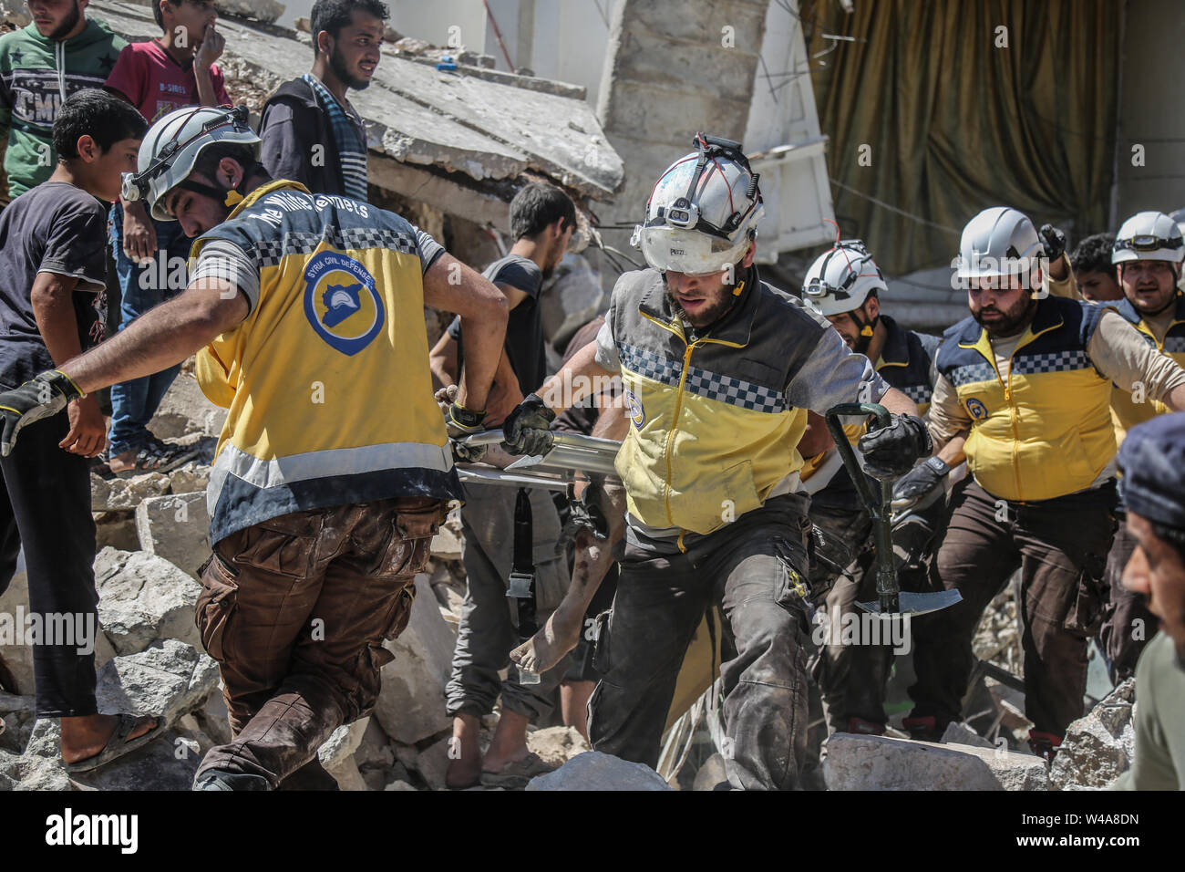 Urm Al Jaws, Syria. 21st July, 2019. Members of the Syrian Civil Defence also known as 'White Helmets' carry a victim after a building collapsed during a reported air strike by pro-regime forces in the town of Urm Al-Jaws in the south of Syria s Idlib Credit: Anas Alkharboutli/dpa/Alamy Live News Stock Photo