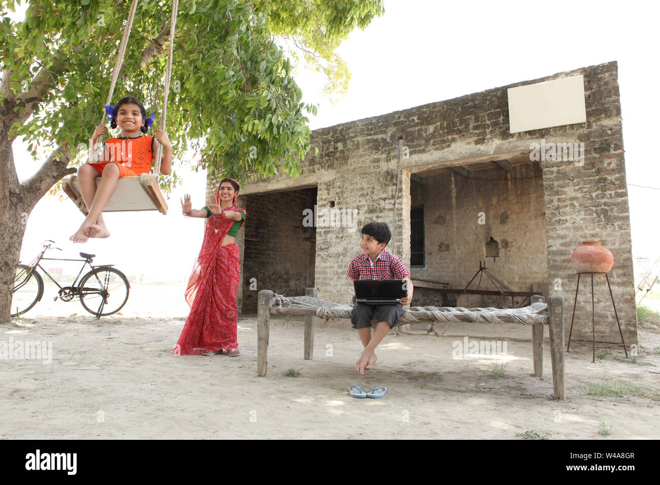 Indian woman pushing her daughter on a rope swing with her son using ...