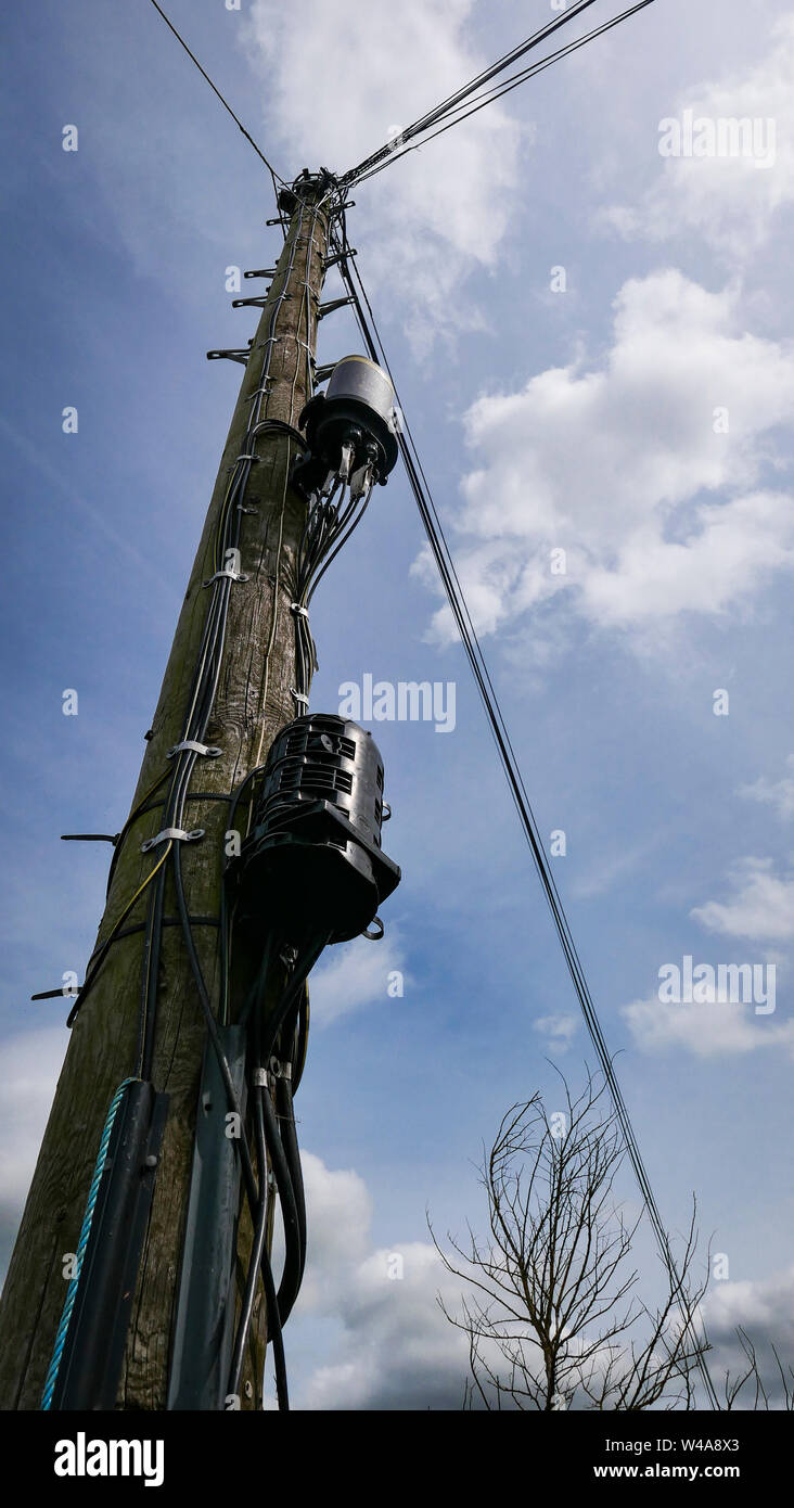 A British wooden telegraph pole against a blue sky with steps, telephone wires and old fashioned electrical components. Stock Photo