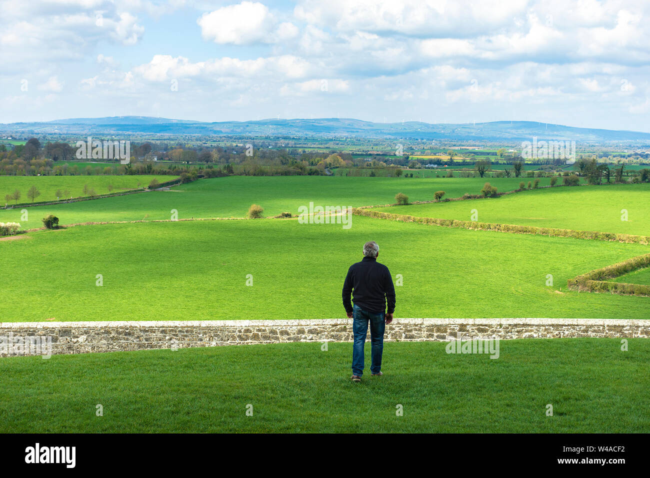 Middle-aged man with dark clothes, walking across a field, before to jump a wall, a stone fence. Overcome difficulties. Walk facing towards. Looking a Stock Photo