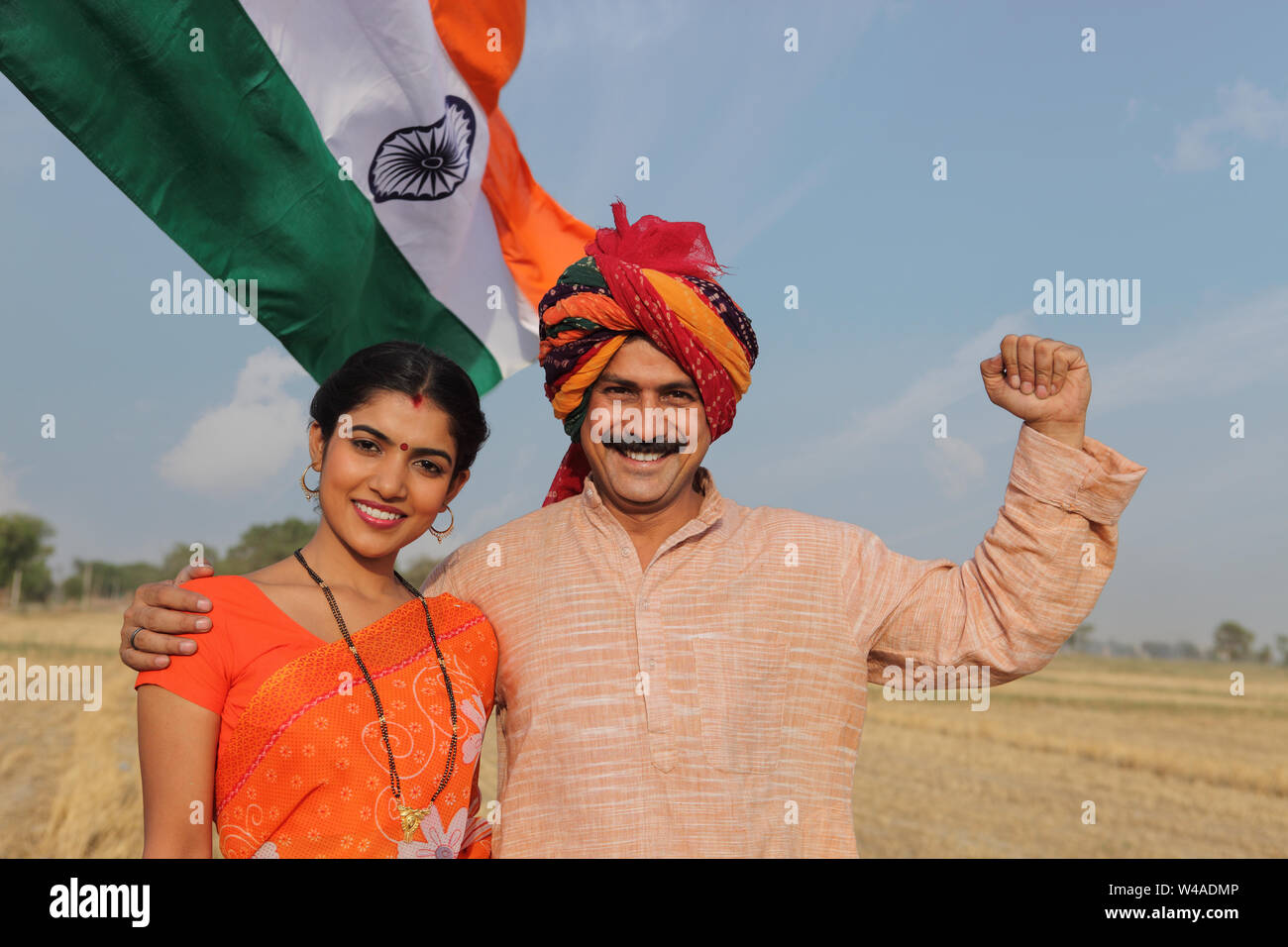 Portrait of a rural couple smiling with Indian flag in the background ...