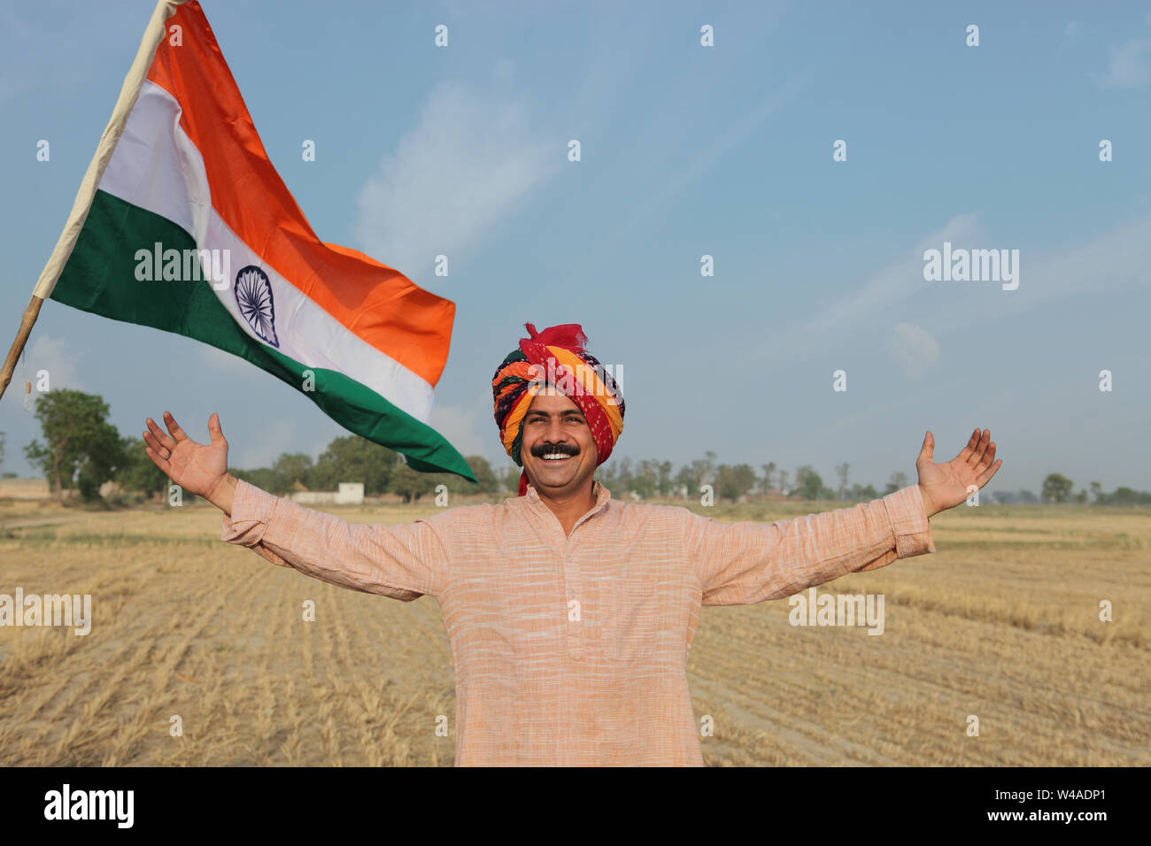 Farmer smiling in a harvested crop field with Indian flag in the ...