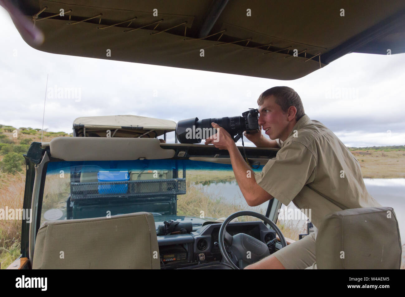 male game ranger using a professional camera and taking a photo of African wildlife while sitting on the door of the safari 4x4 game drive vehicle Stock Photo