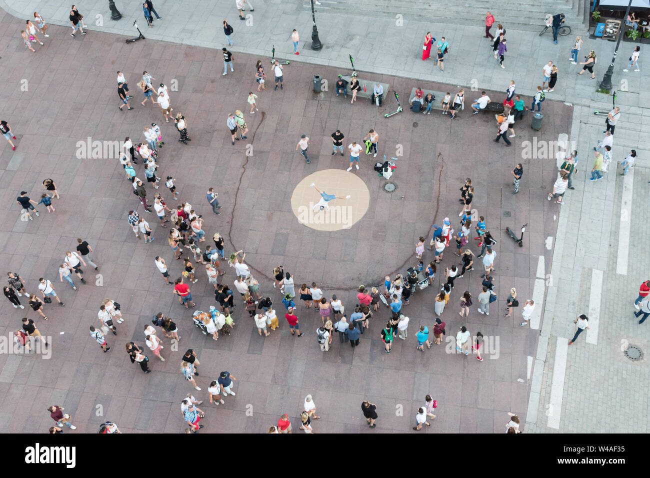 A crowd gathers in a pedestrianised area near Castle Square in Warsaw, Poland, as a street performer performs acrobatics on his hands. Stock Photo