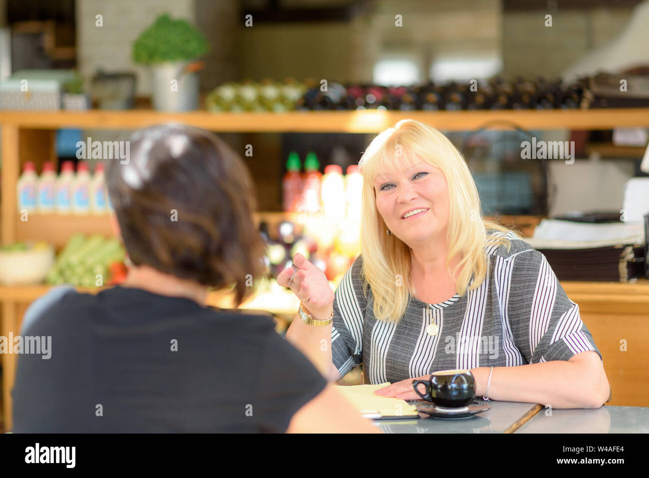 Two happy smiling girlfriends having a cup of coffee in coffee house. Psychologist with patient in cafe. Portrait of middle aged woman professional re Stock Photo
