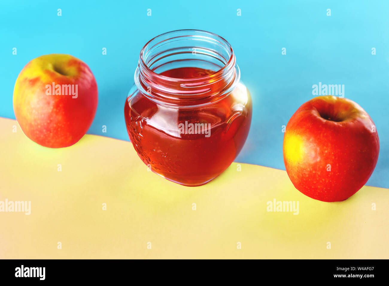 Two apples and honey jar over blue yellow background. Healthy food