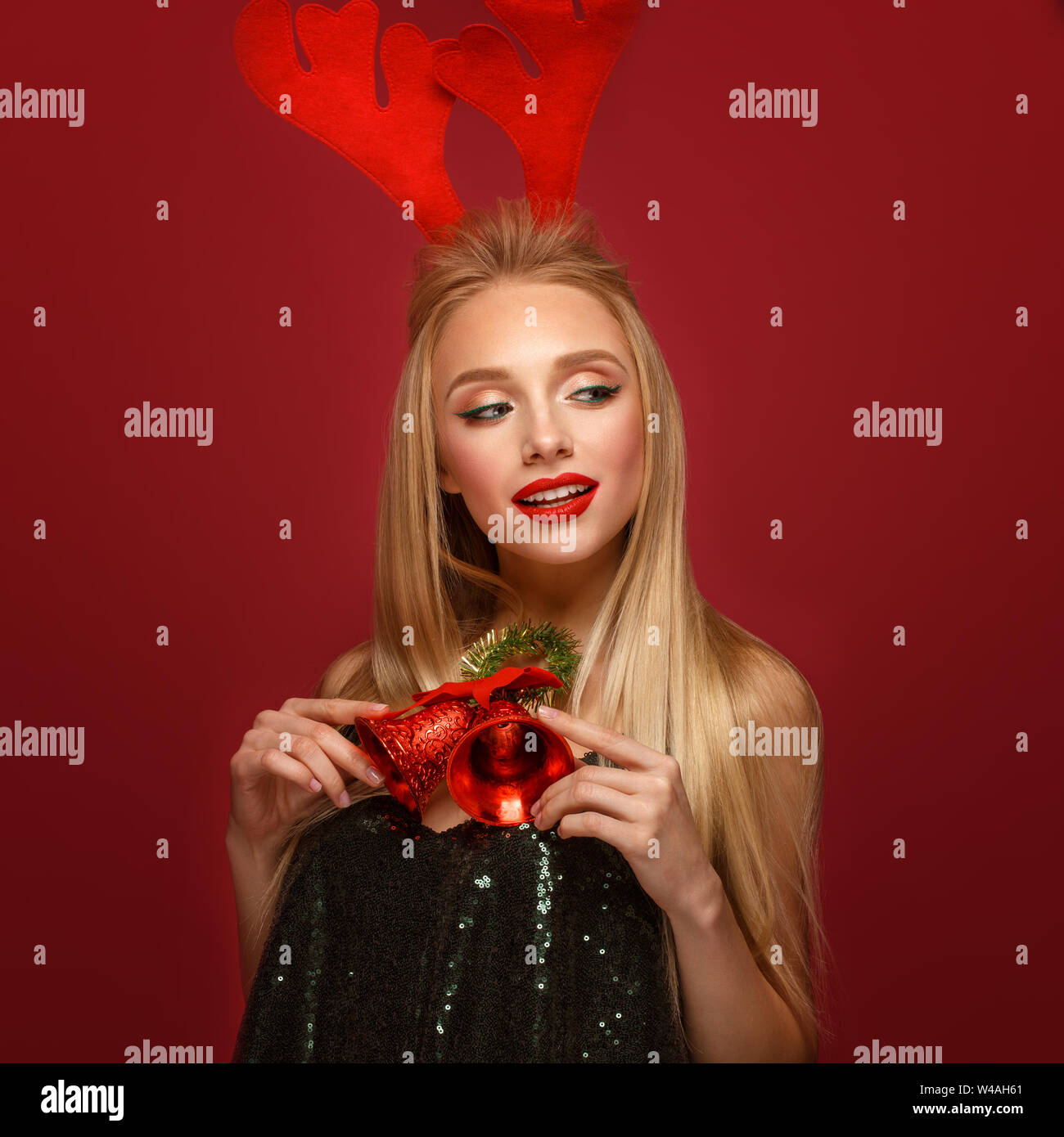 Beautiful blonde girl in a New Year's image with Christmas bells around her neck and deer horns on her head. Beauty face with festive makeup. Photo ta Stock Photo
