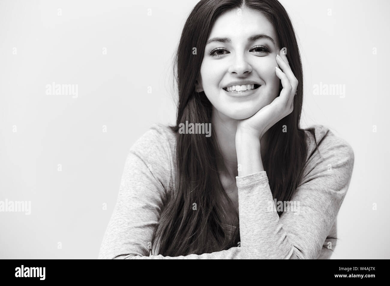 black and white portrait of a beautiful caucasian woman, hand on cheek, looking at camera smiling Stock Photo