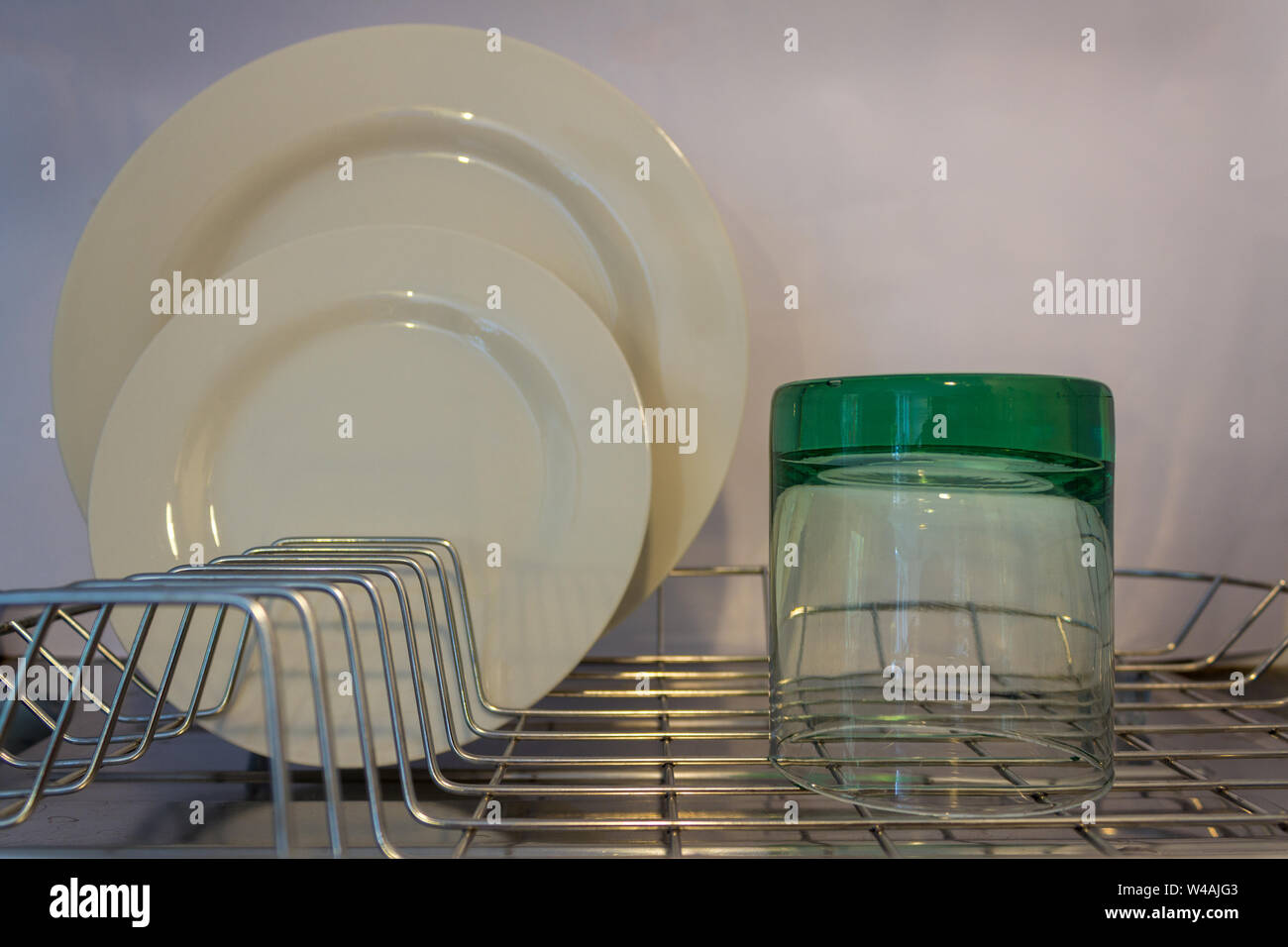 A glass tumbler on a wire drainer with a dinner plate and a smaller side plate in the background Stock Photo