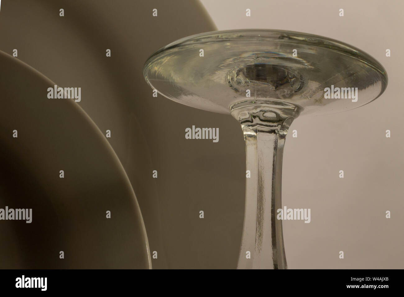 close-up details of the base of an inverted wine glass drying on a drainer next to two white plates Stock Photo