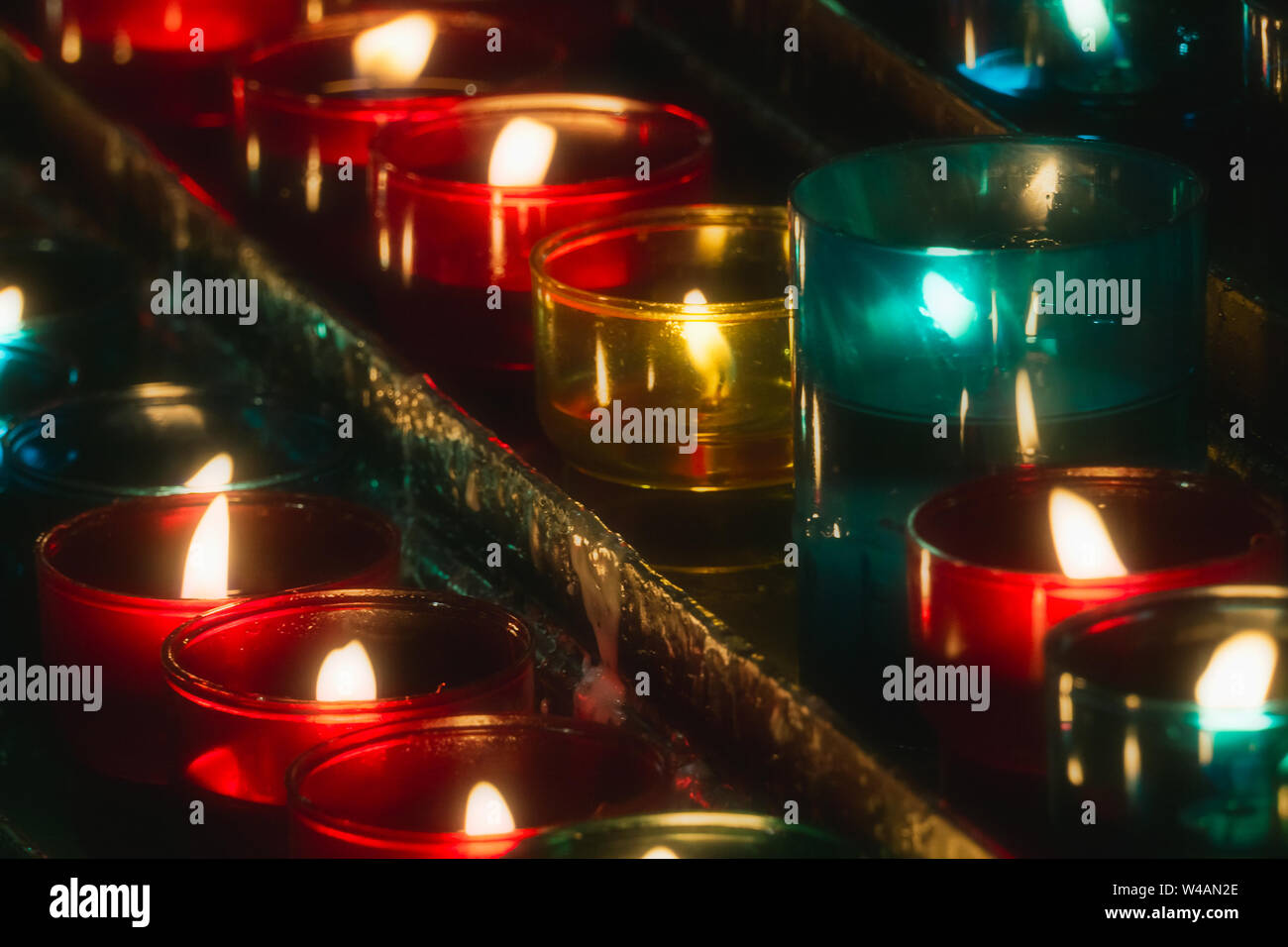 Closeup of rows of candles burning in multicolored glass tealights in a church. Stock Photo