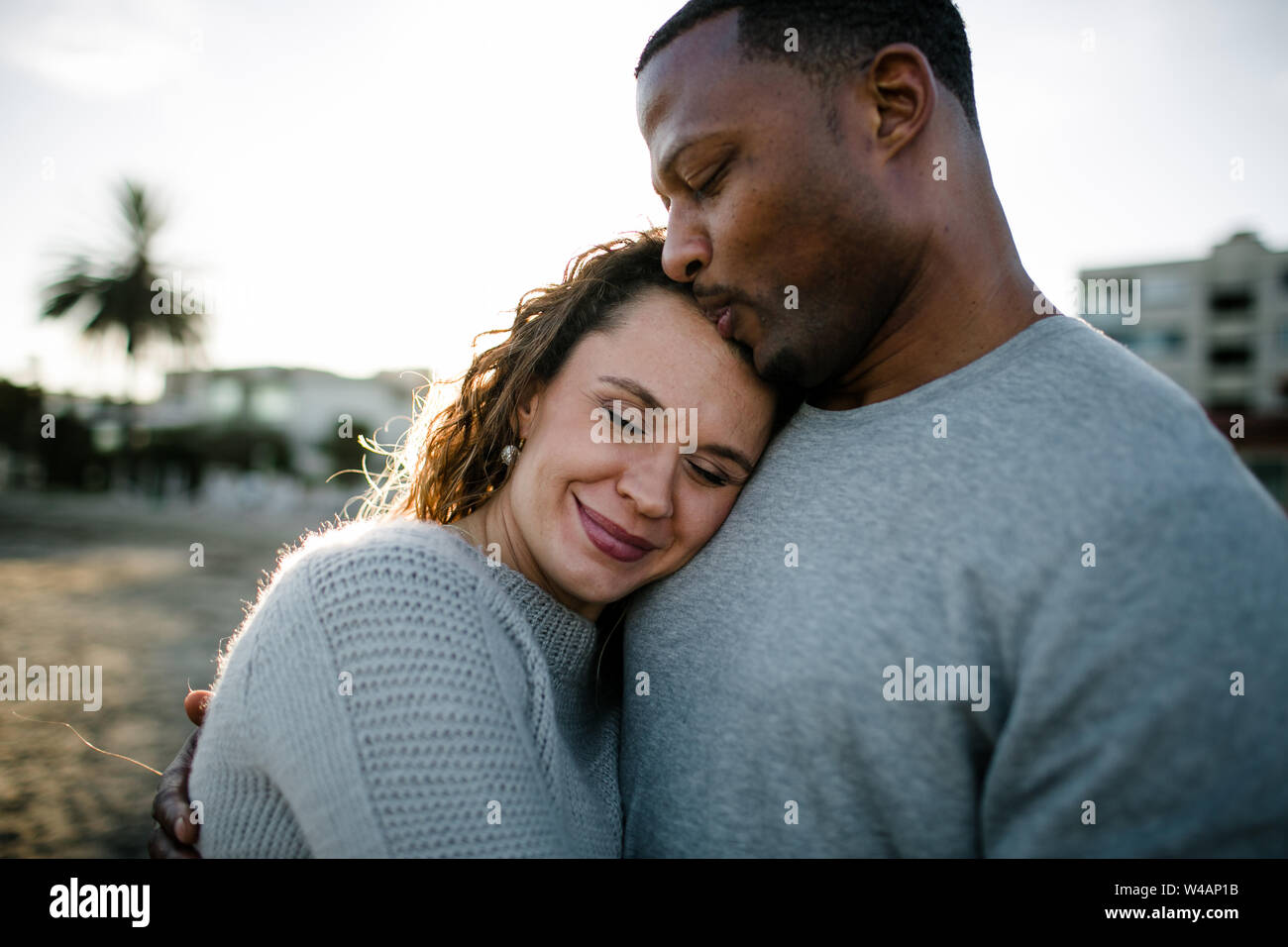 Multi racial couple embrace on beach at sunset Stock Photo