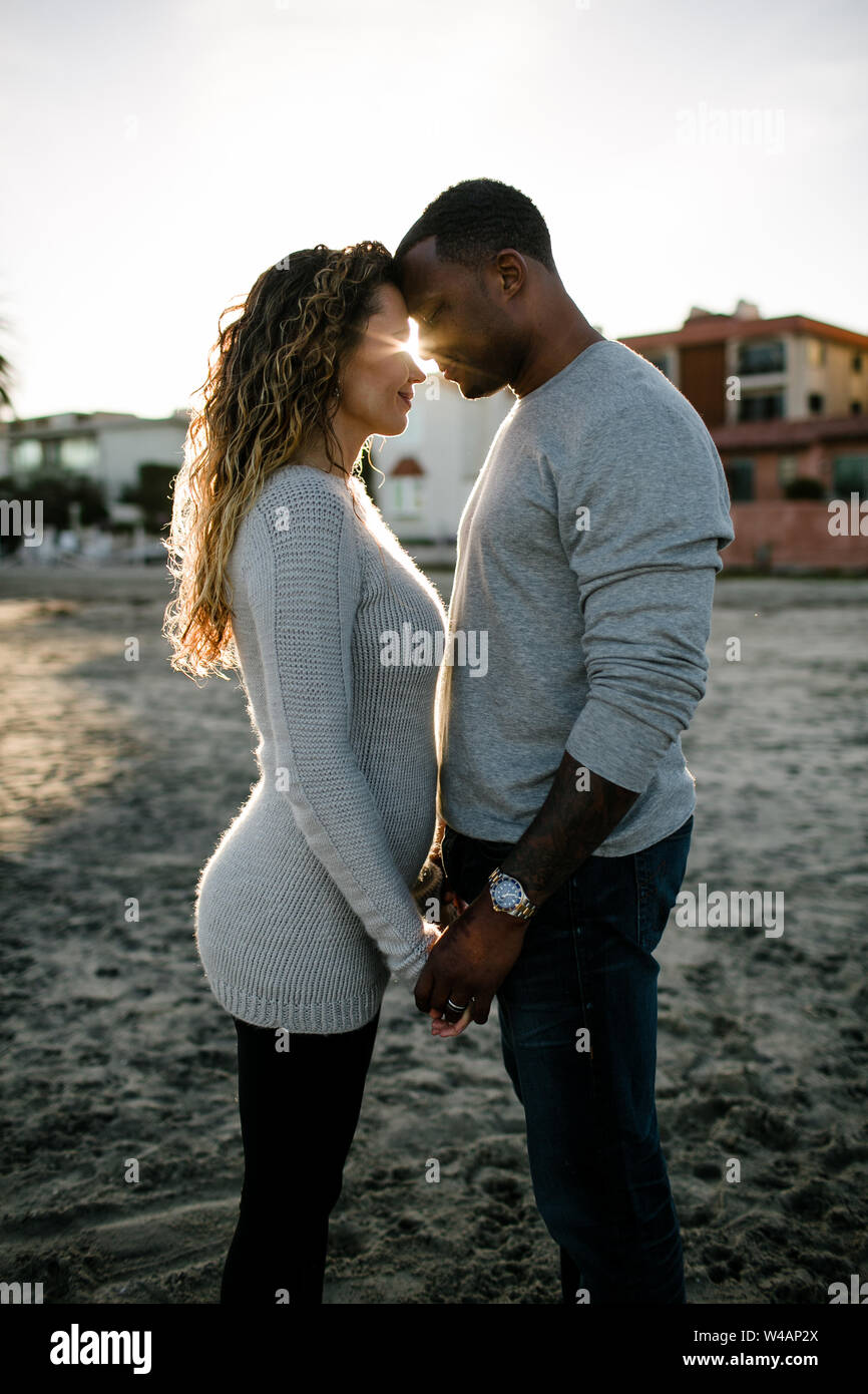 multi racial couple embrace on beach at sunset Stock Photo
