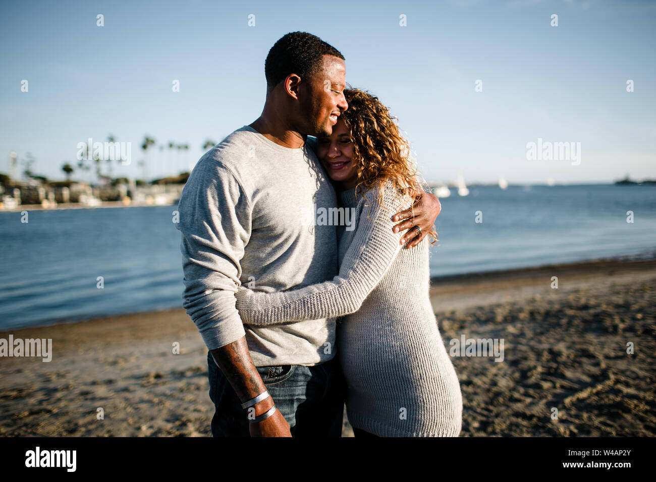 Multi racial couple embrace on beach at sunset Stock Photo - Alamy