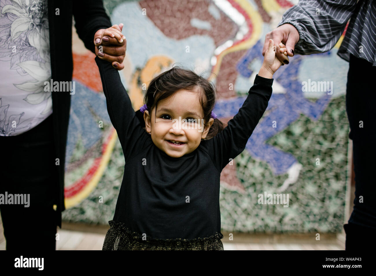 Little girl smiling & holding hands in front of color mural Stock Photo